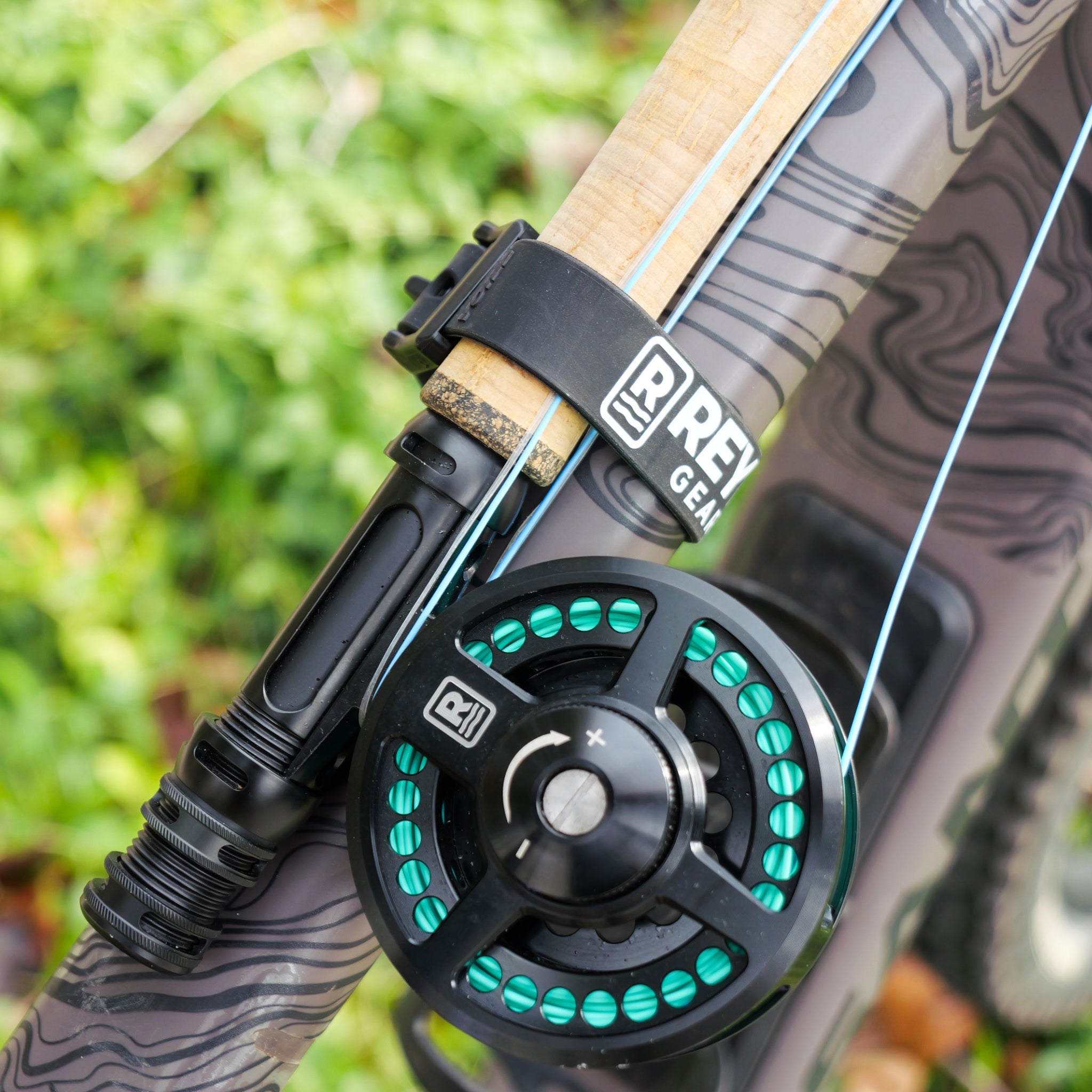 Close-up of a fishing reel attached to a rod with a blurred green background