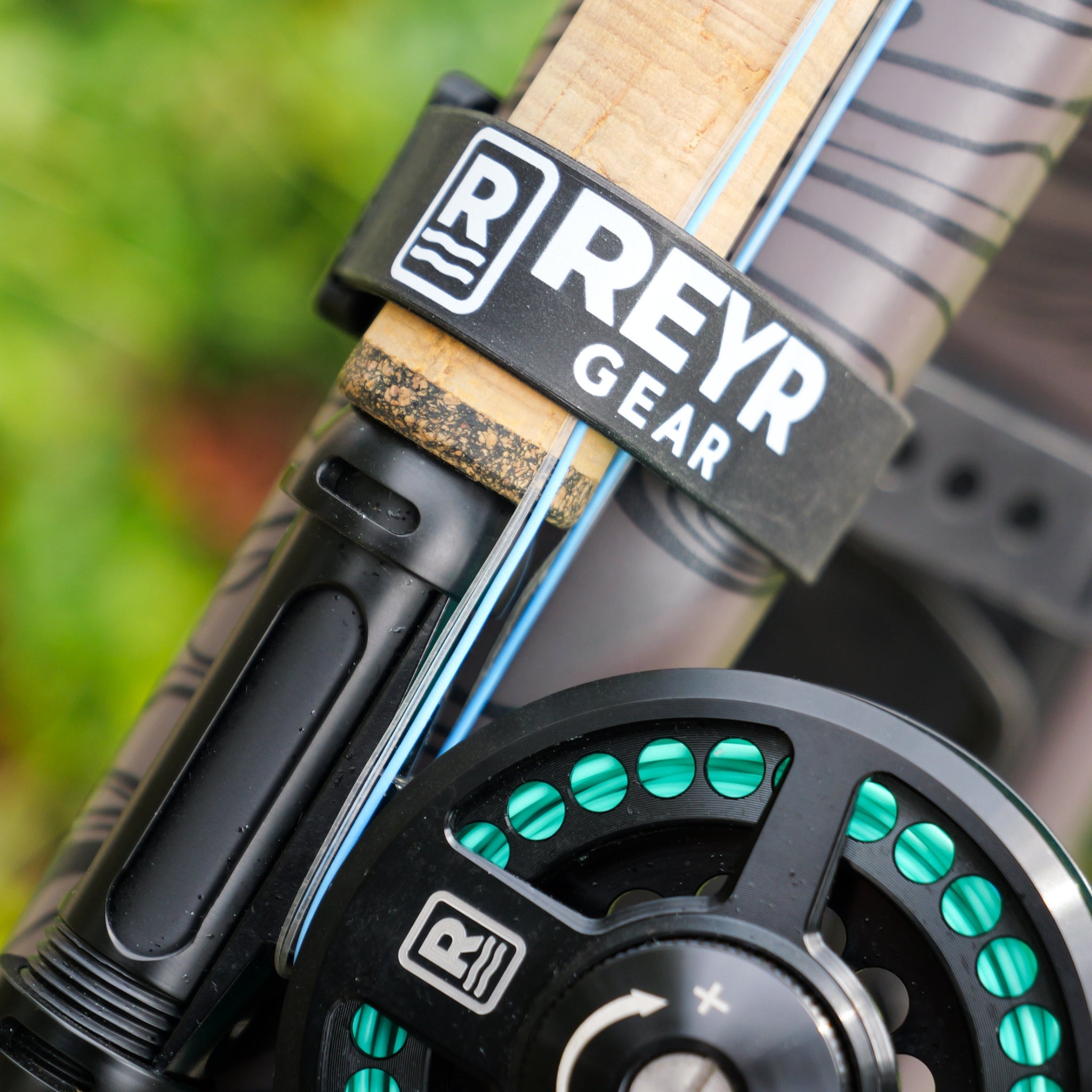Fishing reel with REYR Gear branding on a blurred natural background
